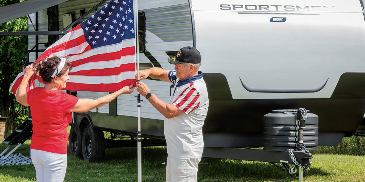 2025 KZ RV Sportsmen SE 292RBKSE Travel Trailer with Couple Raising USA Flag at Campground